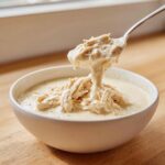 A spoonful of shredded chicken coated in thick cream of chicken soup being lifted from a white bowl.