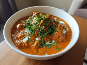 A close-up of a rich, orange pumpkin curry served in a white bowl, garnished with fresh cilantro.