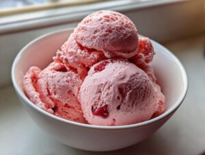 Close-up of several scoops of pink strawberry ice cream with visible fruit pieces in a white bowl.