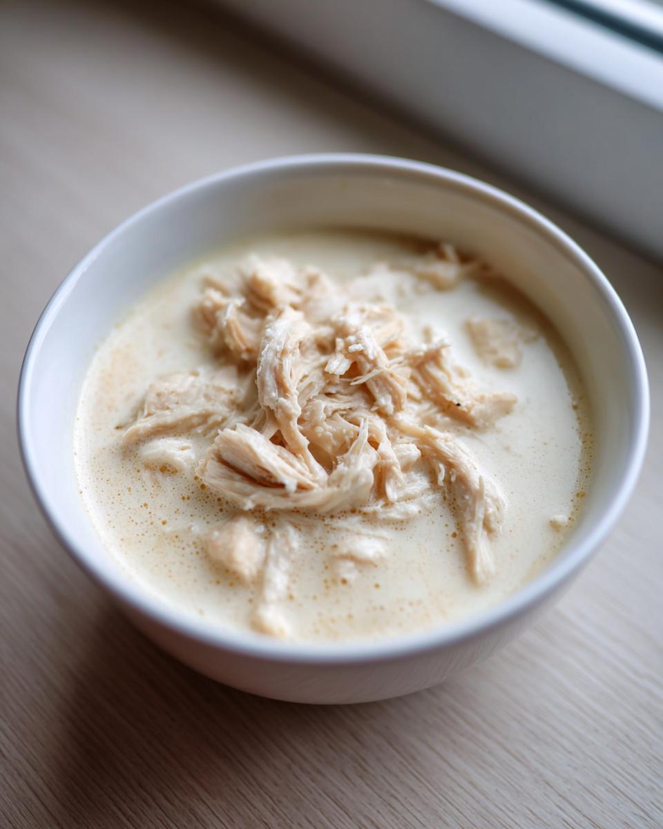 A close-up of shredded chicken served in a creamy white bowl of homemade cream of chicken soup.