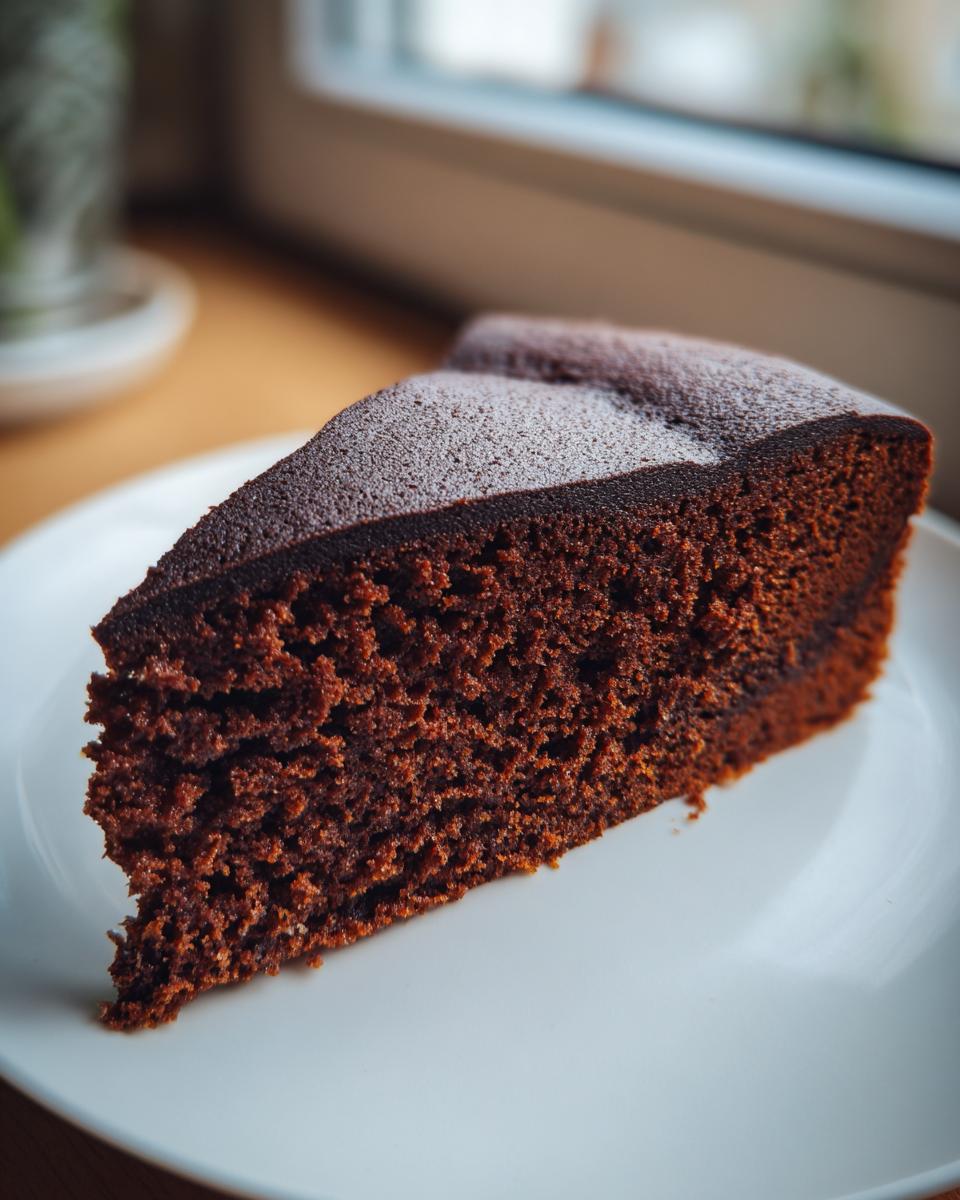 A close-up of a rich, dark slice of chocolate cake recipe on a white plate.