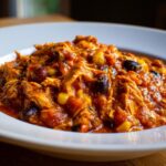 Close-up of a hearty serving of slow cooker buffalo chicken chili, featuring shredded chicken, black beans, and corn in a rich sauce.
