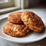 Close-up of three soft, chewy snickerdoodle cookies generously coated in cinnamon sugar, resting on a white plate.