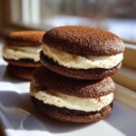 Two stacked chocolate tiramisu cookies filled with creamy mascarpone frosting and dusted with cocoa powder.