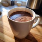 Close-up of a steaming white mug filled with rich, dark crockpot hot chocolate recipe on a wooden surface.
