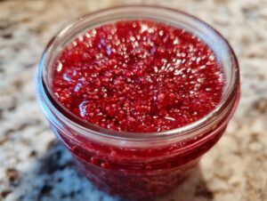 Close-up view of vibrant red strawberry freezer jam filling a clear glass jar, showing texture and seeds.
