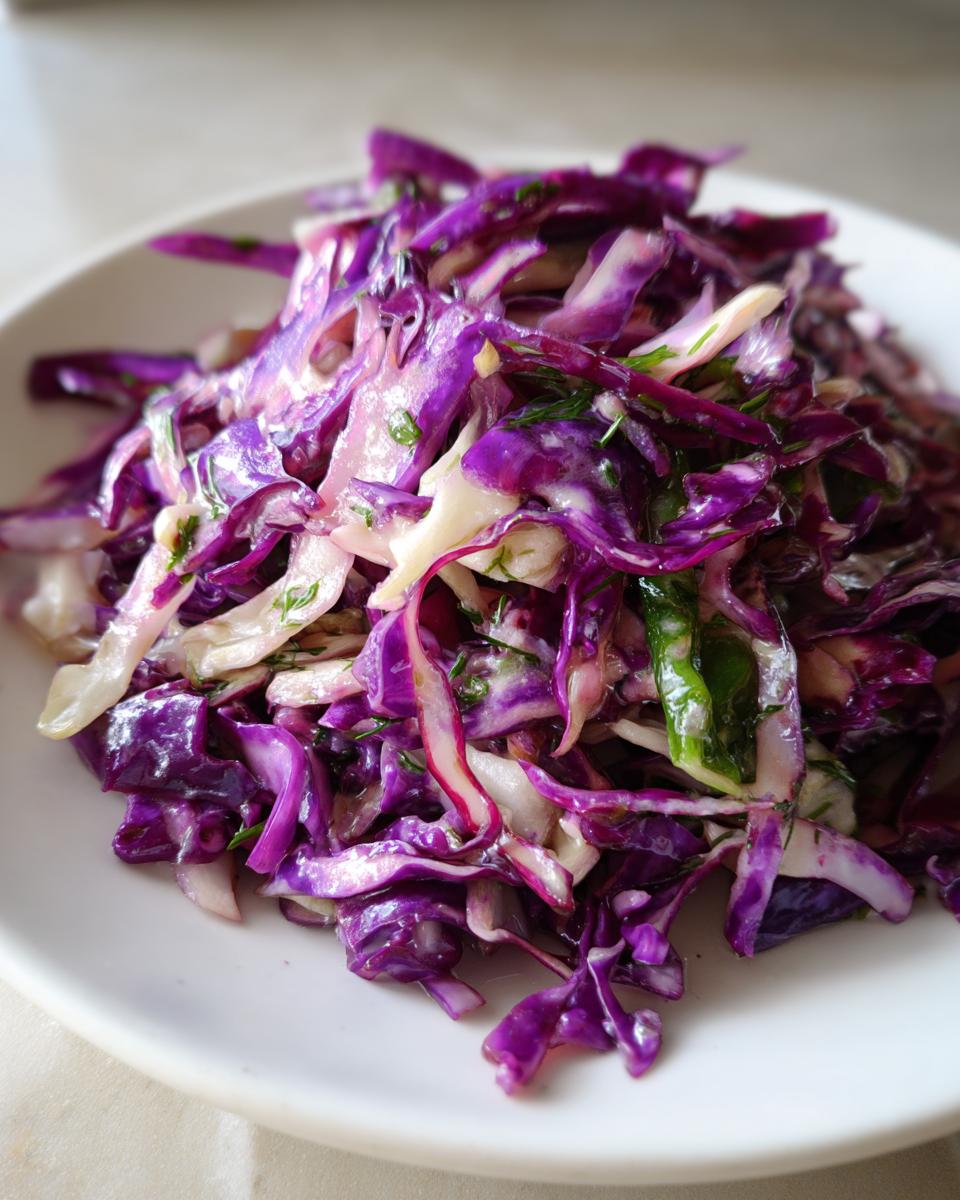 Close-up of a vibrant red cabbage salad tossed in a light dressing with visible herbs, served on a white plate.