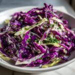 Close-up of a vibrant red and white cabbage salad tossed with herbs, ready to eat.