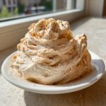A generous swirl of light brown cinnamon butter, dusted with cinnamon powder, served on a small white plate.
