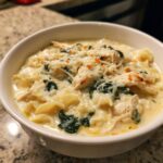 Close-up of a hearty bowl of white chicken lasagna soup topped with shredded cheese and spinach.