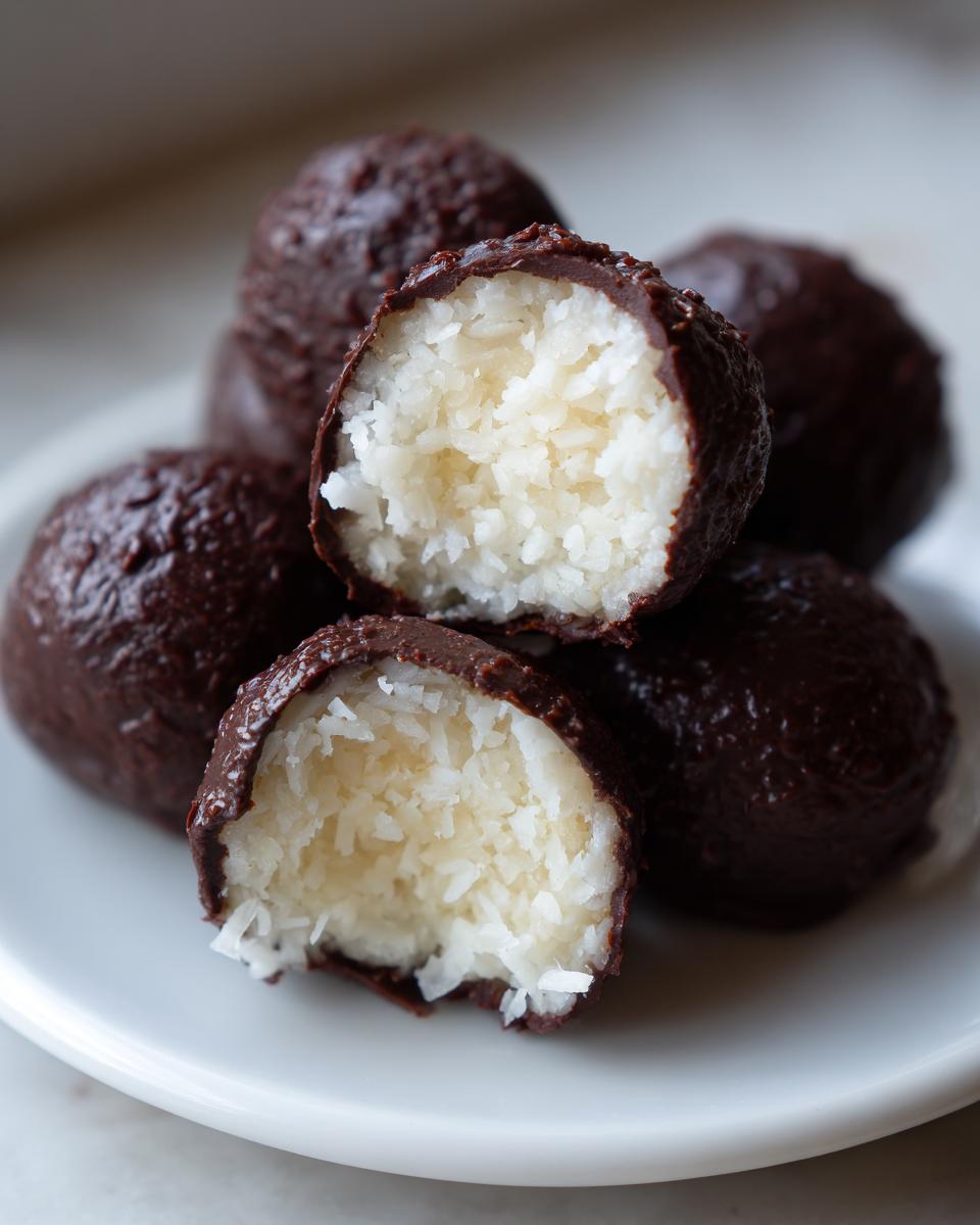Close-up of chocolate-coated almond joy truffles, one cut in half showing the shredded coconut filling.