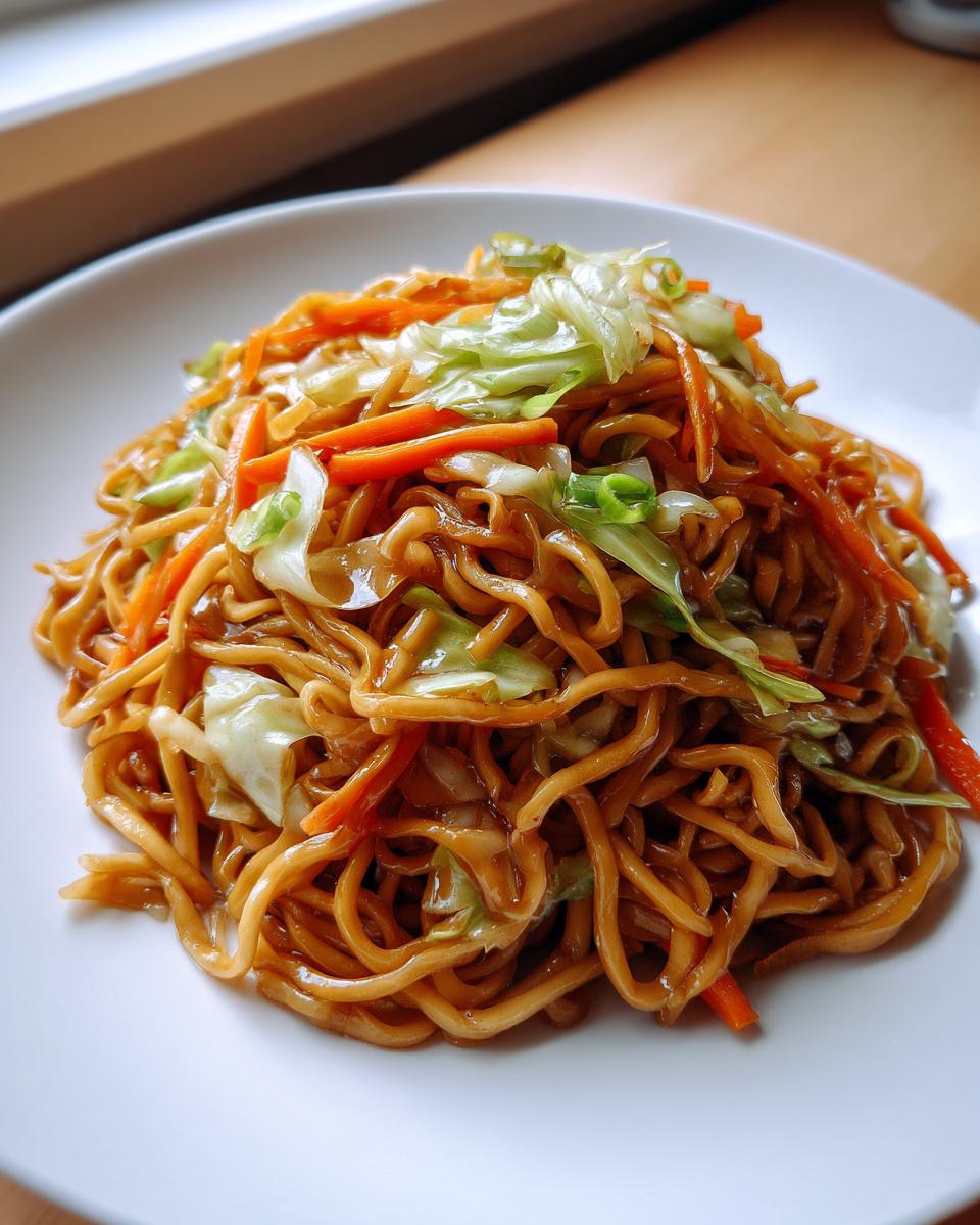 A close-up shot of a mound of glossy, saucy fried noodles topped with shredded cabbage and carrots.