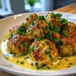 Close-up of golden-brown chicken piccata meatballs served in a creamy lemon-caper sauce and topped with fresh parsley.