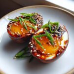 Two halves of glossy, brown marinated eggs with jammy yolks, topped with sesame seeds and scallions.