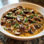 A close-up of rich, creamy mushroom sauce filled with sliced brown mushrooms and topped with fresh parsley.