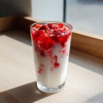 A tall glass of homemade strawberry milk layered with fresh, bright red strawberry pieces and milk.