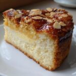 Close-up of a moist slice of bee sting cake showing the vanilla cream filling and caramelized almond topping.
