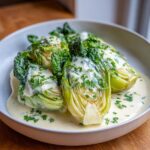 Close-up of tender braised leeks covered in a rich white wine sauce and sprinkled with fresh parsley.