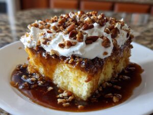 A decadent slice of butter pecan praline poke cake topped with whipped cream and pecans, sitting in a pool of caramel sauce.