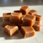 A pile of freshly cut, chewy homemade caramel squares sitting on a light surface.