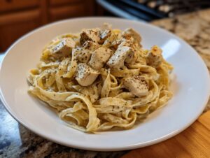 A close-up of creamy chicken fettuccine alfredo tossed in sauce and topped with seasoned chicken pieces.