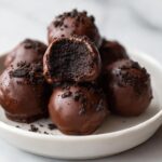 A stack of rich, chocolate-dipped Oreo balls, one cut in half showing the dark, dense interior.