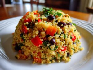 A close-up of a perfectly molded portion of cilantro lime quinoa salad featuring red peppers and black beans on a white plate.