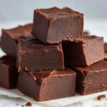 A close-up stack of rich, dark chocolate 3-ingredient fudge squares resting on white parchment paper.