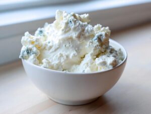 A white bowl generously filled with chunky, creamy blue cheese dip ingredients, ready for mixing.