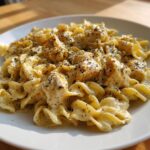 Close-up of a serving of creamy chicken pasta coated in a rich sauce and heavily seasoned with black pepper.