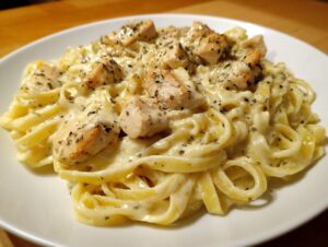Close-up of creamy chicken pasta featuring fettuccine noodles coated in a rich white sauce and topped with seasoned chicken pieces.