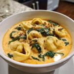 Close-up of a hearty bowl of creamy tortellini soup featuring cheese tortellini, wilted spinach, and red pepper flakes.