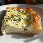 A thick, square slice of rich white pizza topped with creamy ricotta cheese, olive oil, and fresh parsley.