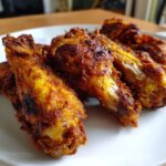 Close-up of several golden-brown, seasoned crispy baked chicken wings piled on a white plate.