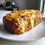 A whole loaf of crockpot french onion meatloaf topped with melted, gooey cheese on a white plate.