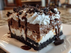A rich slice of layered chocolate and vanilla ice cream cake topped with whipped cream, chocolate sauce, and cookie crumbs.
