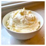 A white bowl filled with freshly whipped, fluffy vanilla buttercream frosting, showing soft peaks.