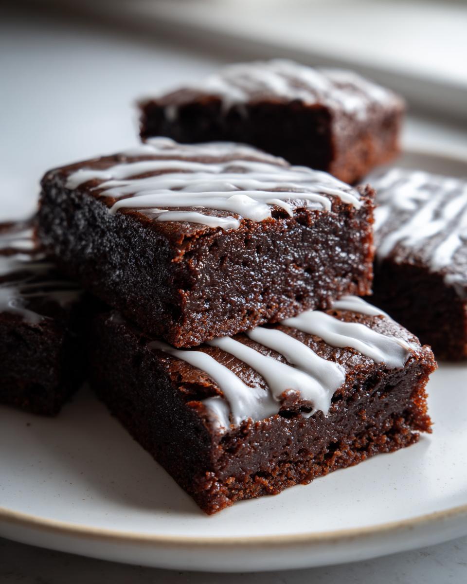 Close-up of fudgy, dark chocolate gingerbread brownies topped with white icing drizzle.