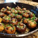 Close-up of whole, sautéed garlic butter mushrooms glistening in butter and topped with fresh parsley in a cast iron skillet.