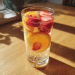 A tall glass filled with bubbly champagne punch, garnished with bright orange slices and fresh strawberries.