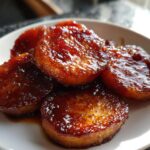 Close-up of perfectly glazed, thick-cut southern candied yams piled on a white plate.