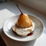 A single, beautifully caramelized poached pears resting on a swirl of whipped cream, drizzled with syrup.