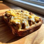 Close-up of a single slice of toast topped with savory ground meat mixture and melted cheese, ready to eat as a hanky panky recipe.