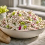 A close-up of a creamy bowl of cottage cheese chicken salad mixed with bright green celery and purple red onion pieces.