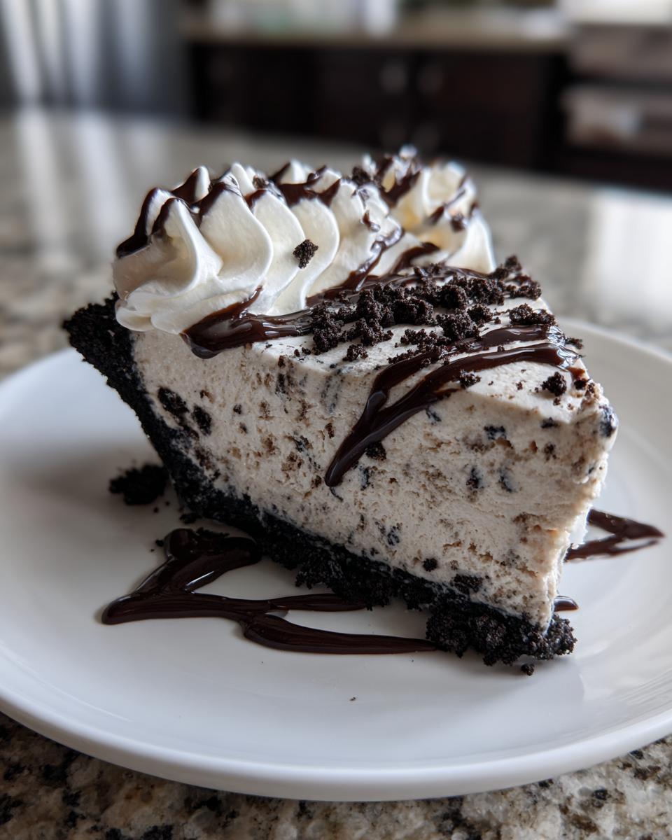 A decadent slice of cookies and cream ice cream pie with whipped cream and chocolate syrup on a white plate.