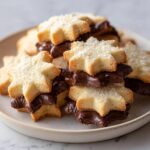 A stack of star-shaped Italian butter cookies filled and dipped in rich dark chocolate, dusted with sugar.