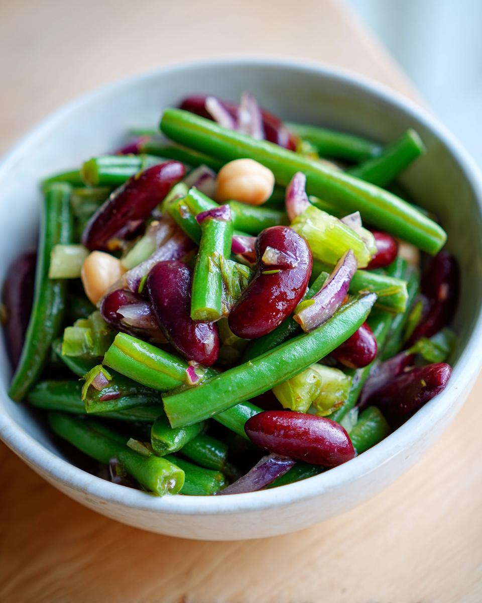 Close-up of a bowl filled with a vibrant bean salad featuring green beans, kidney beans, and chickpeas.
