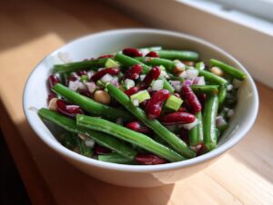 A white bowl filled with a vibrant bean salad featuring green beans, kidney beans, and chopped onions.