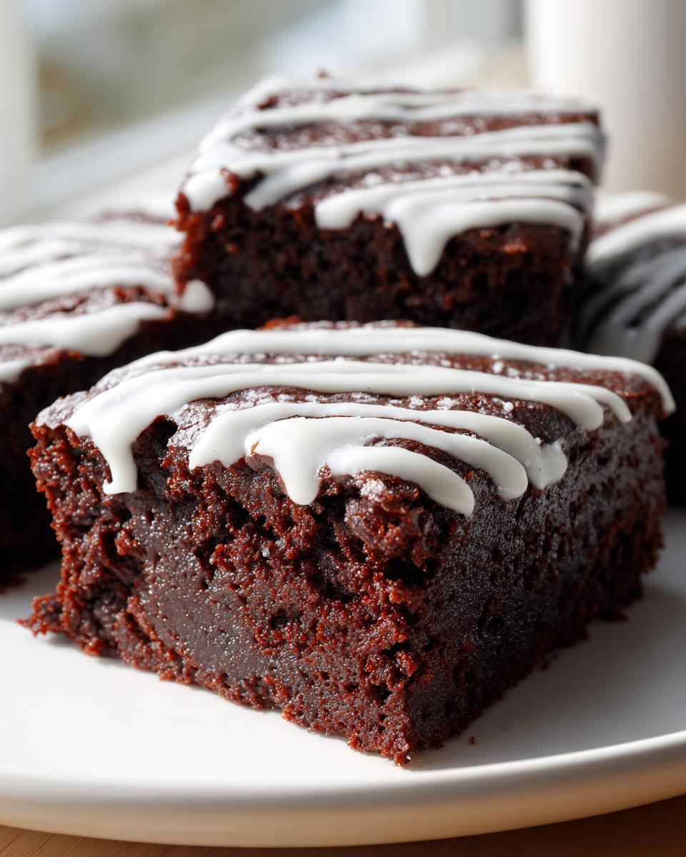 Close-up of fudgy gingerbread brownies topped with a white vanilla icing drizzle on a white plate.