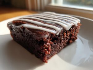 Close-up of a rich, dark gingerbread brownie square topped with a drizzle of white vanilla icing.